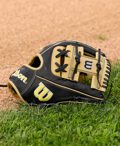 A Wilson A2000 1786 11.5" Baseball Glove (WBW104108115) in black and tan with H-Web construction lies on green grass by the dirt infield.