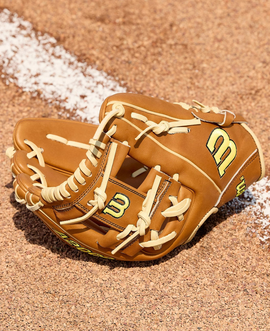 A Wilson A2000 DP15 11.5" Baseball Glove (WBW104111115) with cream laces rests on a sandy field beside a white chalk baseline.