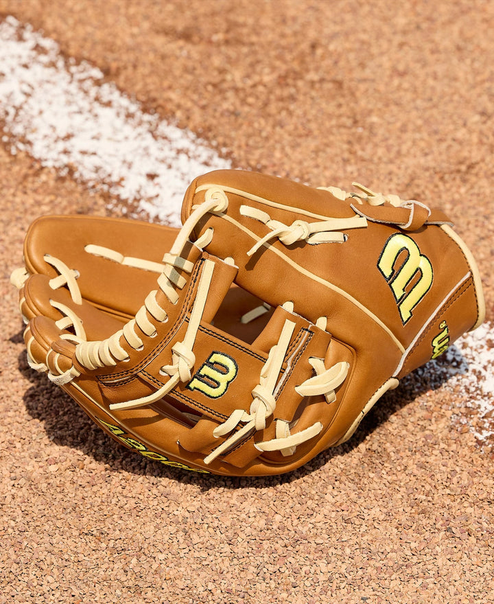 A Wilson A2000 DP15 11.5" Baseball Glove (WBW104111115) with cream laces rests on a sandy field beside a white chalk baseline.