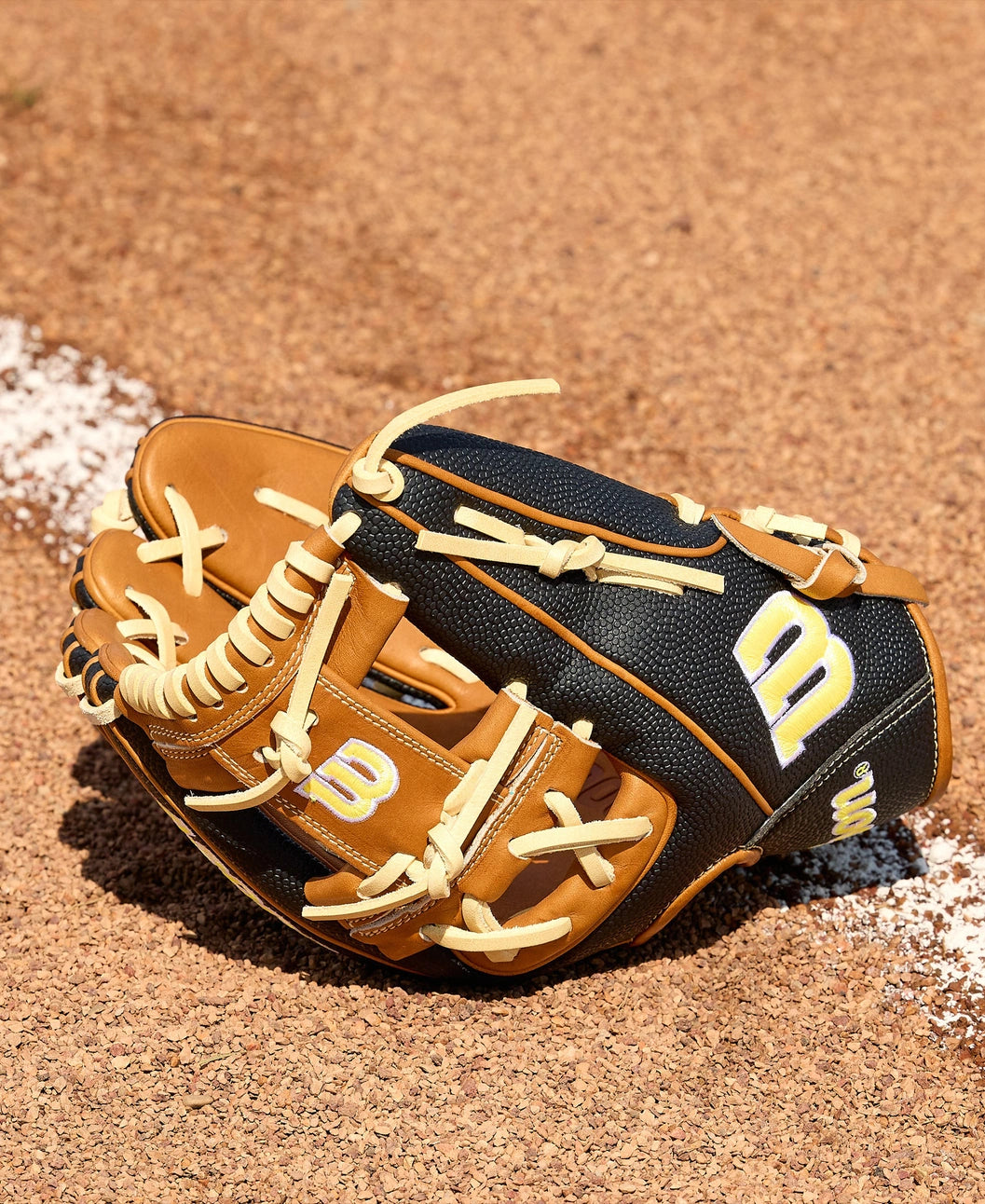 A Wilson A2000 1975SS 11.75" baseball glove (WBW1041121175), featuring brown and black leather with cream laces and a yellow-and-white W logo, rests on infield dirt near a white chalk line, showcasing SuperSkin durability.