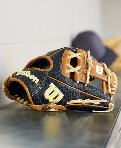 A Wilson A2000 1975SS 11.75" baseball glove (WBW1041121175) by Wilson, featuring black and tan leather with cream laces, sits on a metal dugout surface with a blurred cap visible in the background.