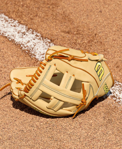 A Wilson A2000 EL3 11.75" Baseball Glove (WBW1041141175) by Wilson, featuring a tan design with brown laces, lies open on sandy dirt beside a white chalk foul line on the baseball field.