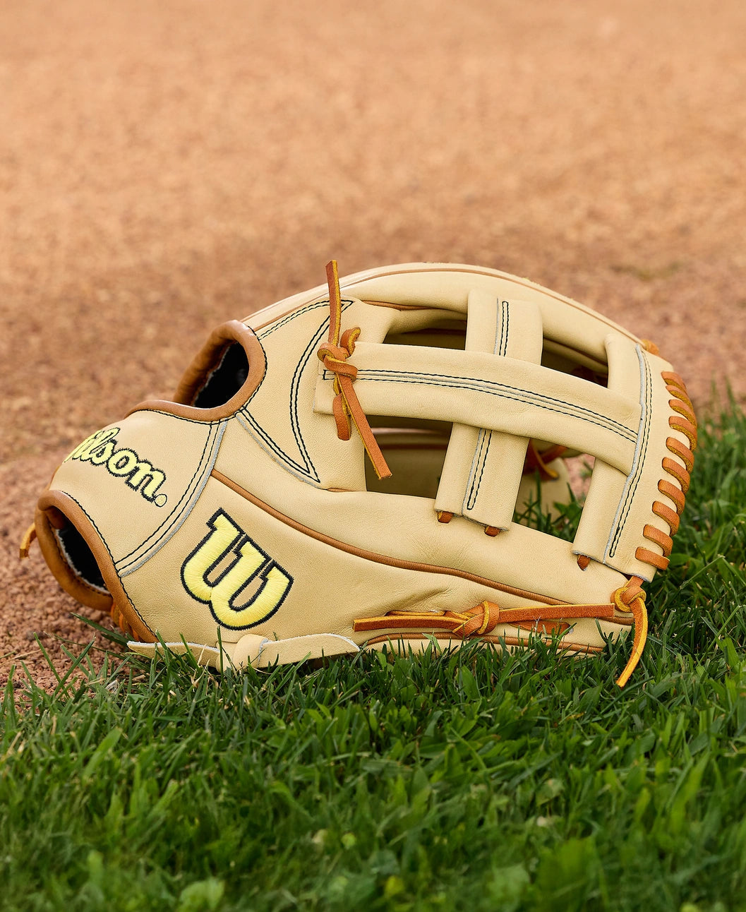 A Wilson A2000 EL3 11.75" Baseball Glove (WBW1041141175) with Pro Stock Leather and brown laces lies on green grass beside the baseball field dirt.