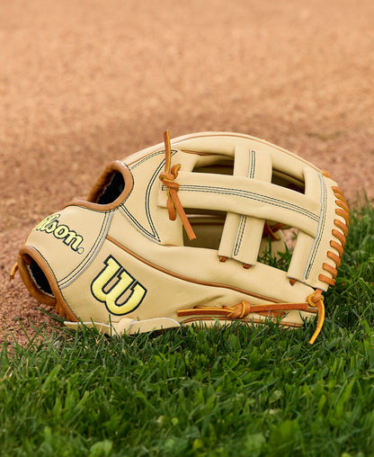 A Wilson A2000 EL3 11.75" Baseball Glove (WBW1041141175) with Pro Stock Leather and brown laces lies on green grass beside the baseball field dirt.