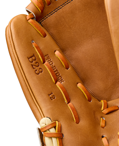 Close-up of a Wilson A2000 B23 12" Baseball Glove with brown Pro Stock leather, tan and orange laces, visible stitching, and embossed text: B23, PRO-STOCK, and 12. Model: WBW10411712.