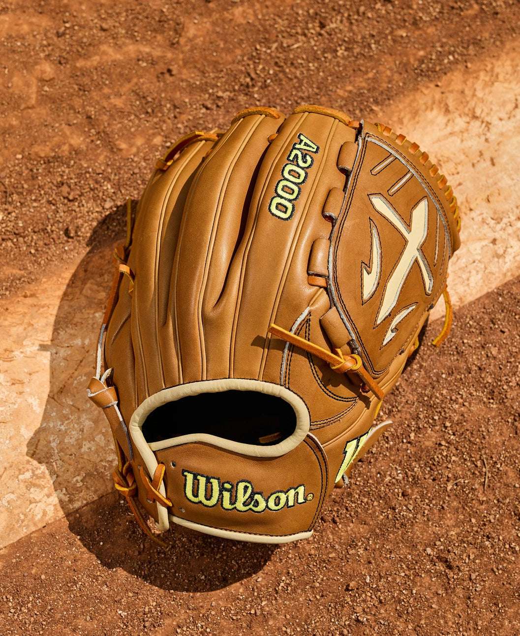 A Wilson A2000 B23 12" Baseball Glove (WBW10411712) by Wilson lies on a dirt field, partially covering a white chalk baseline.