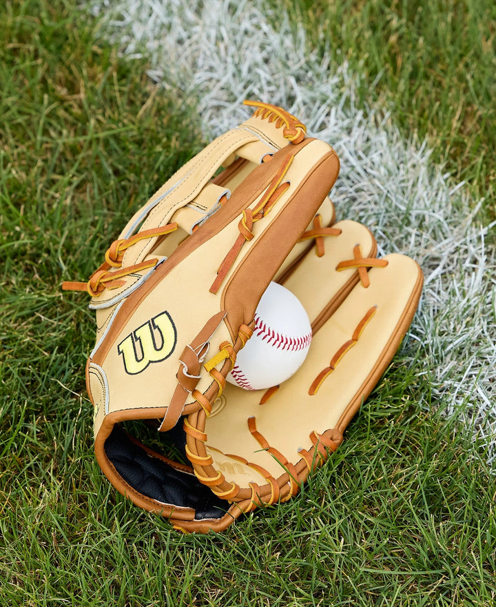 A Wilson A2000 1777 12.75" Baseball Glove (WBW1041251275) in tan holds a white baseball on green grass by a chalk line, highlighting the Pro Stock Leather quality from Wilson.