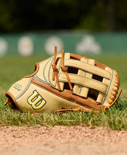 The Wilson A2000 1777 12.75" Baseball Glove (WBW1041251275) by Wilson, shown in tan and brown on grass and dirt with a blurred field, features Pro Stock Leather for lasting durability and classic style.