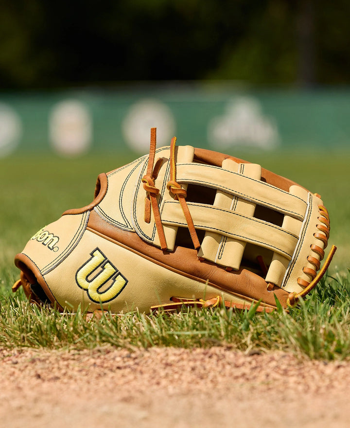 The Wilson A2000 1777 12.75" Baseball Glove (WBW1041251275) by Wilson, shown in tan and brown on grass and dirt with a blurred field, features Pro Stock Leather for lasting durability and classic style.