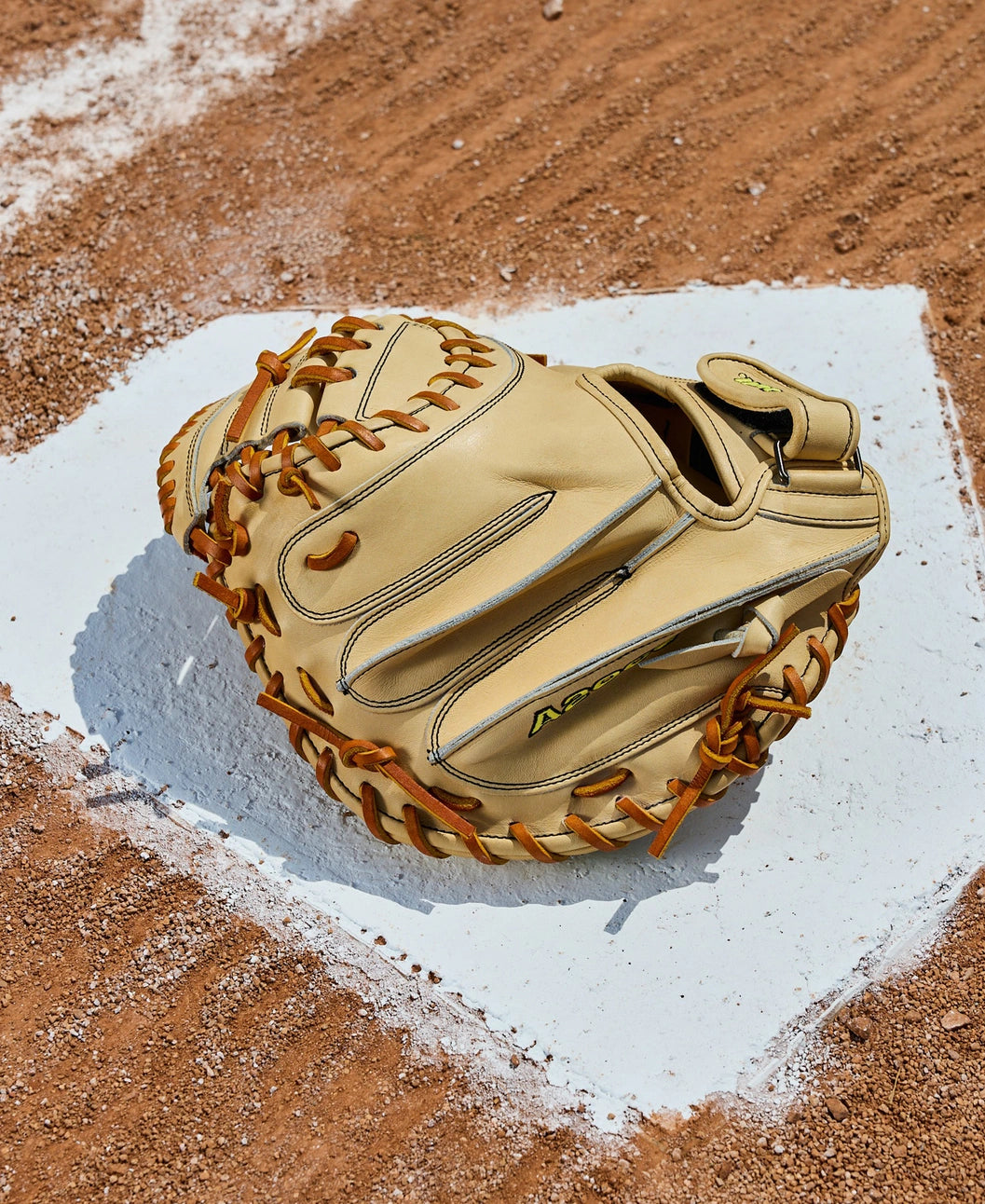 A Wilson A2000 PF33 33" Baseball Catcher's Mitt (WBW10412733) with brown laces rests on home plate, its tan Pro Stock Leather standing out against the reddish-brown dirt of the baseball field.