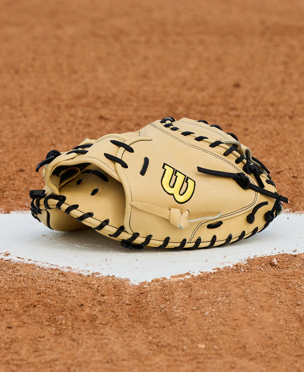 A Wilson A2000 1734 34" Baseball Catcher's Mitt (WBW10412934) by Wilson in tan and black sits on the pitcher’s mound, displayed on a dirt field with white chalk lines visible beneath.