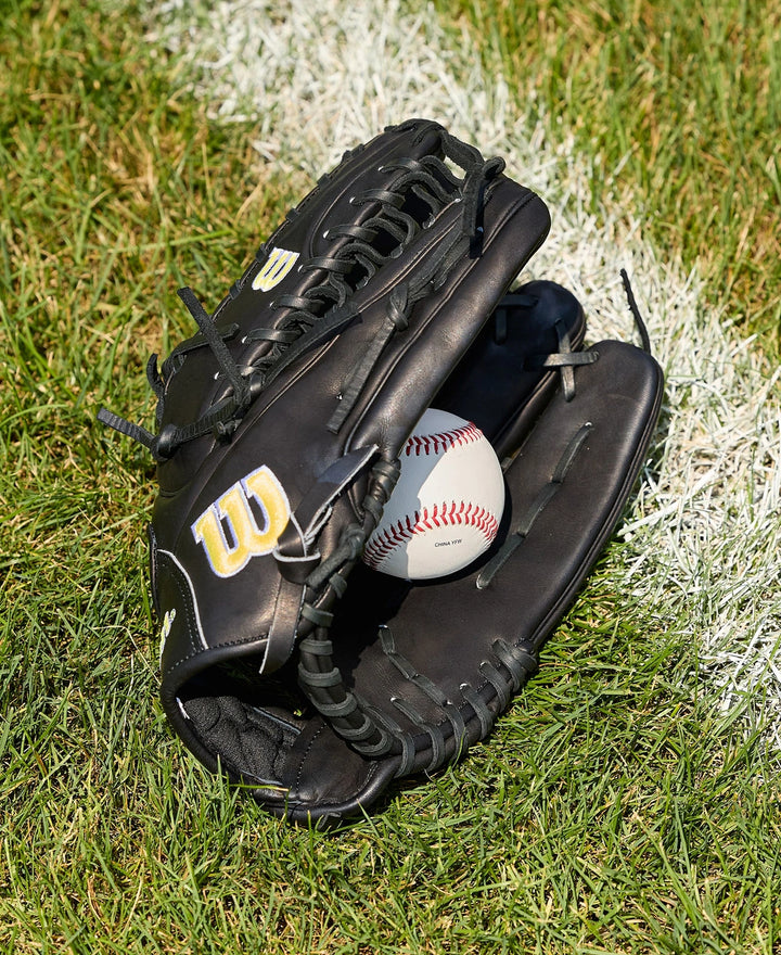 A black Wilson A2000 OT7 12.75" Baseball Glove (WBW1041811275), clutching a white baseball, sits on green grass near a white chalk line, with Pro Stock Leather ensuring durability and top performance.