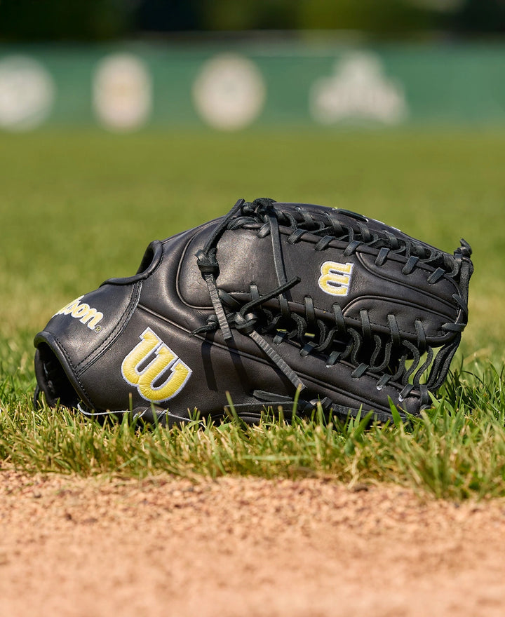 A Wilson A2000 OT7 12.75" Baseball Glove (WBW1041811275) by Wilson, crafted with Pro Stock Leather, sits on green grass near a dirt infield, set against a blurred baseball field background.