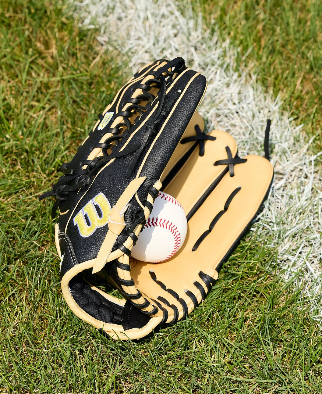 A Wilson A2000 OT7SS 12.75" Baseball Glove (WBW1041831275) by Wilson, in black and tan, holds a baseball as it rests on green grass beside a white chalk line on the field.