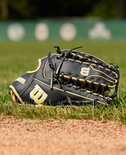 A Wilson A2000 OT7SS 12.75" Baseball Glove (WBW1041831275) by Wilson rests on the grass near the infield dirt, with a blurred green outfield fence and logos in the background.