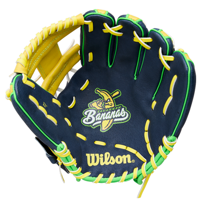 The Wilson A450 Savannah Bananas 11" Youth Baseball Glove (WBW10419211) features navy blue color, yellow and green laces, a cartoon banana with a bat, "Bananas" embroidery on the palm, and a classic H-Web design.