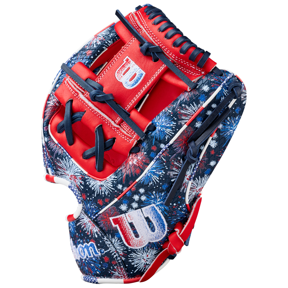 The Wilson A2000 1975SS 11.75" Baseball Glove (GOTM July 2025) features a red, white, and blue fireworks pattern, Pro Stock leather, bold red accents, navy laces, and white W logos on the thumb and wrist.