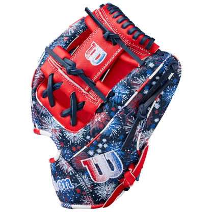 The Wilson A2000 1975SS 11.75" Baseball Glove (GOTM July 2025) features a red, white, and blue fireworks pattern, Pro Stock leather, bold red accents, navy laces, and white W logos on the thumb and wrist.