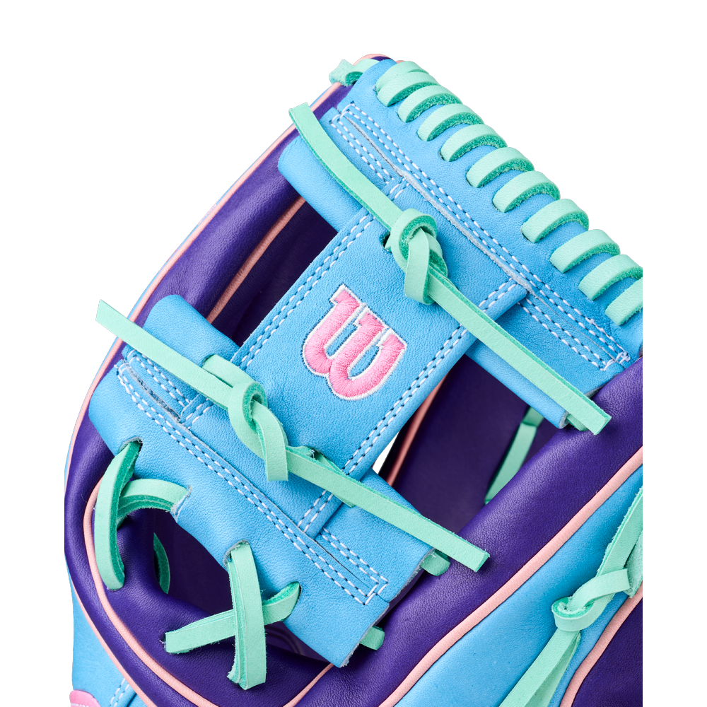 Close-up of the Wilson A2K 1720 11.5" GOTM October 2025 Baseball Glove, showcasing blue, purple, and teal Pro Stock Select leather with green laces and a pink-embroidered W logo on a blue patch.