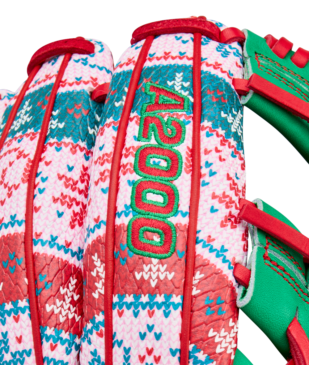 Close-up of the Wilson A2000 1975 11.75" Baseball Glove (GOTM Dec 2025), featuring a colorful holiday red, green, pink, and white woven pattern, green embroidered A2000 text, red laces, green leather accents, and Pro Stock leather.