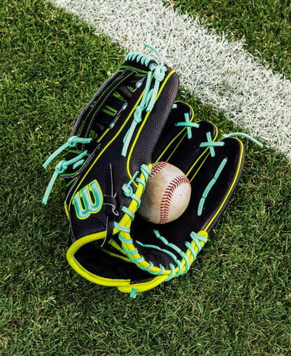 A Wilson A2000 1750SS 12.5" Baseball Glove (WBW104599125) in black with neon green and blue laces rests open on grass near a white line, holding a baseball. Made with premium Pro Stock leather for lasting performance.