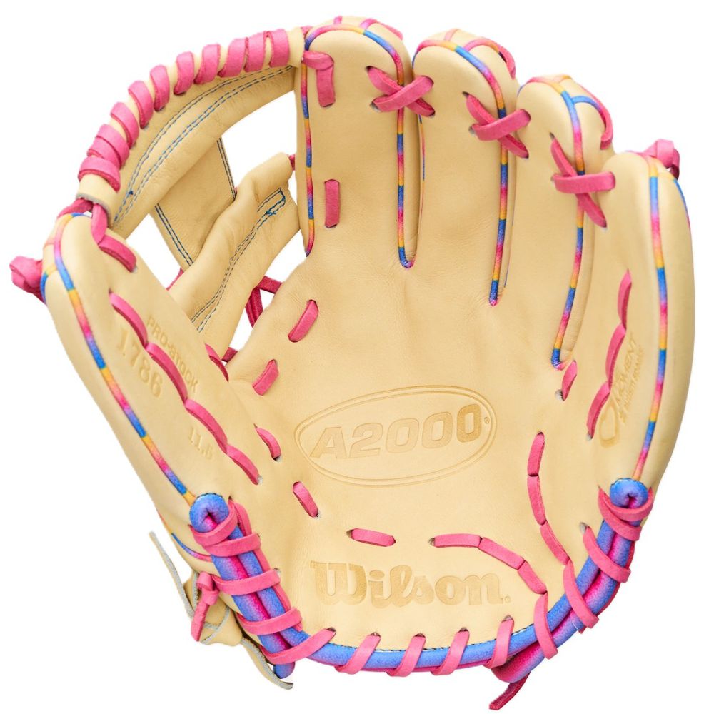 A tan Wilson Love the Moment A2000 1786 11.5" Baseball Glove (WBW104827115) with pink and blue laces, shown palm up. Made from durable Pro Stock Leather, featuring the Wilson logo and model name on the inner palm.