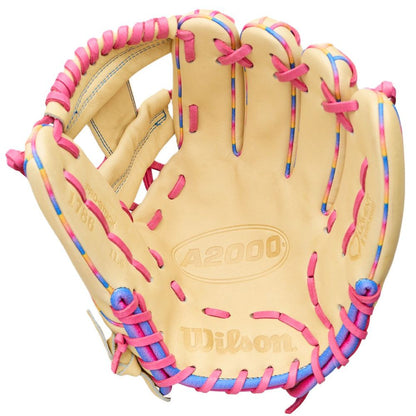 A tan Wilson Love the Moment A2000 1786 11.5" Baseball Glove (WBW104827115) with pink and blue laces, shown palm up. Made from durable Pro Stock Leather, featuring the Wilson logo and model name on the inner palm.
