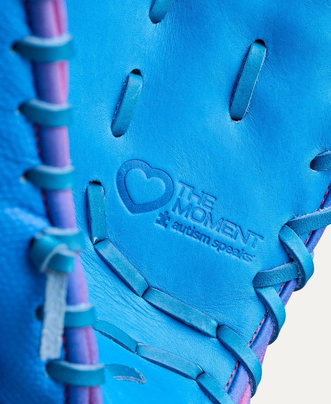 Close-up of a Wilson Love the Moment A2000 1612 12" First Base Mitt (WBW10483812) with blue Pro Stock leather and purple laces. Embossed text reads THE MOMENT and autism speaks, featuring a heart and puzzle piece logo.