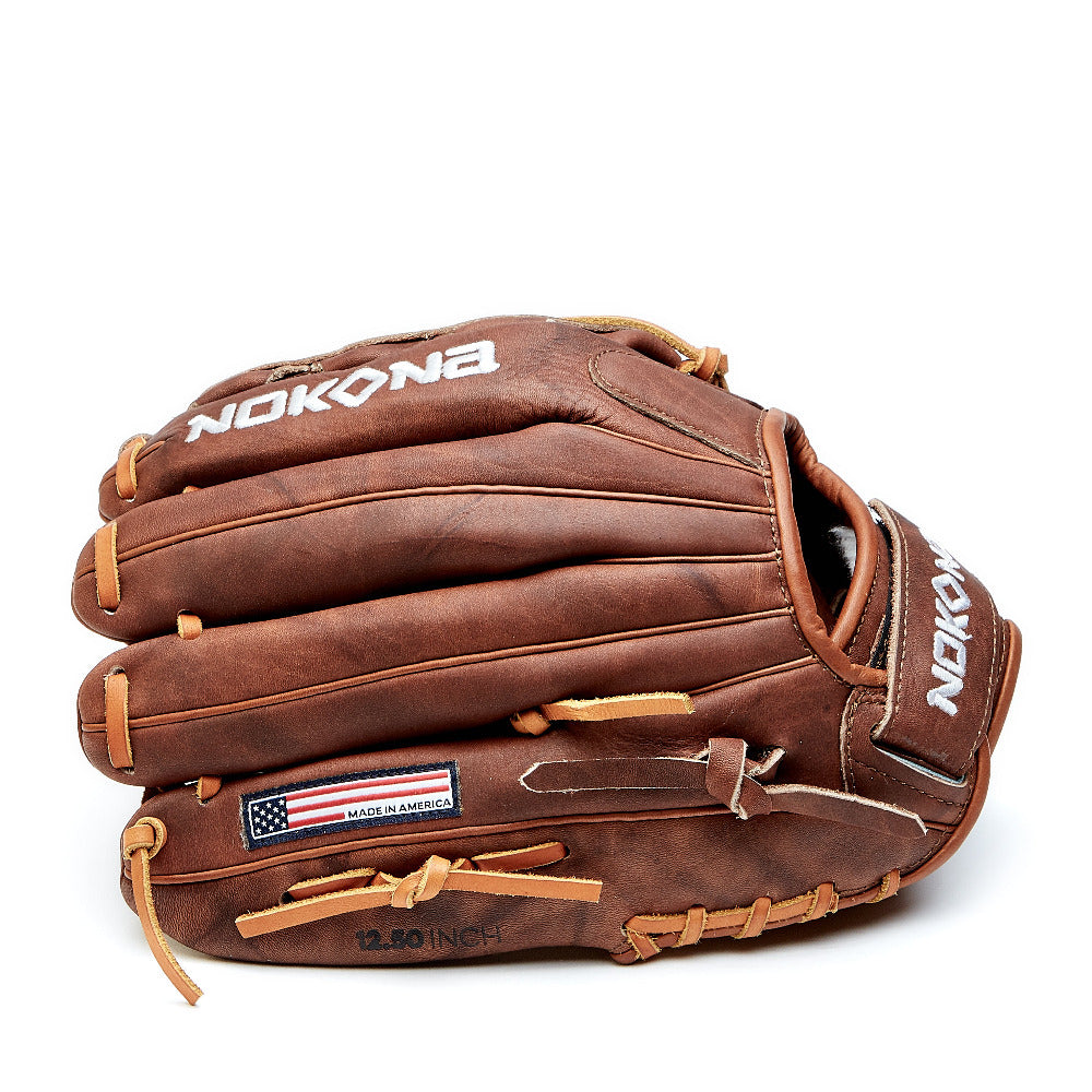 The Nokona Walnut 12" Fastpitch Glove (W-V1200C) features brown Walnut Crunch leather, tan laces, white Nokona logo text, and a USA flag patch labeled "Made in America" above "12.50 Inch" on the side.