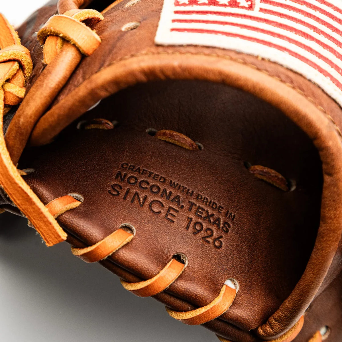 Close-up of a handcrafted Nokona Walnut EP 11.5″ Baseball Glove: W-EP1150 showing the embossed text Crafted with pride in Nocona, Texas since 1926 and a portion of a red and white flag patch.