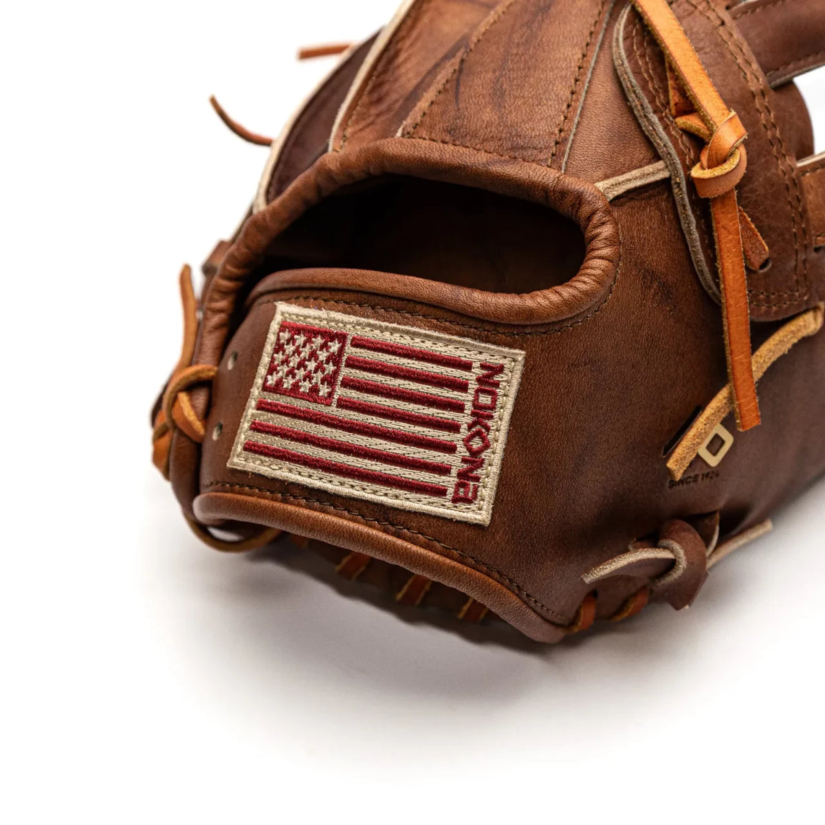 Close-up of a brown leather Nokona Walnut EP 13″ Baseball Glove: W-EP1300H featuring a rectangular patch with a red and white American flag and embroidered text on the wrist strap.