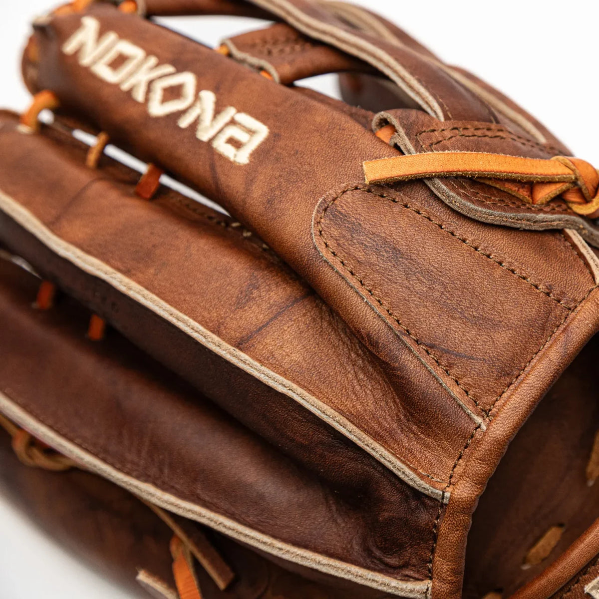 Close-up of a brown Nokona Walnut EP 13″ Baseball Glove: W-EP1300H with tan lacing and a white brand name embroidered on the top.