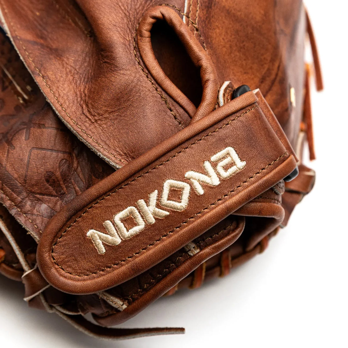 Close-up of a Walnut Crunch Nokona Walnut EP 32.5″ Fastpitch Catcher’s Mitt: W-EPV3250 with the brand name embroidered on the wrist strap.