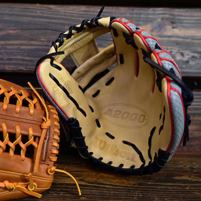 A close-up of two baseball gloves on a wooden surface, with the open Wilson A2000 glove showing stitching details and the model number PP88 inside its tan leather palm.