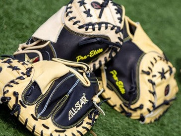 Two tan and black baseball catcher’s mitts with Pro-Elite and All-Star branding rest on green artificial turf.
