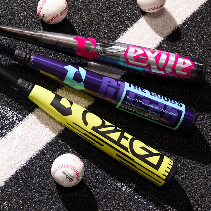 Three colorful baseball bats with bold graphics, labeled EXILE, THE GOODS, and ZOA, are lying on an asphalt surface with white stripes, surrounded by three baseballs.