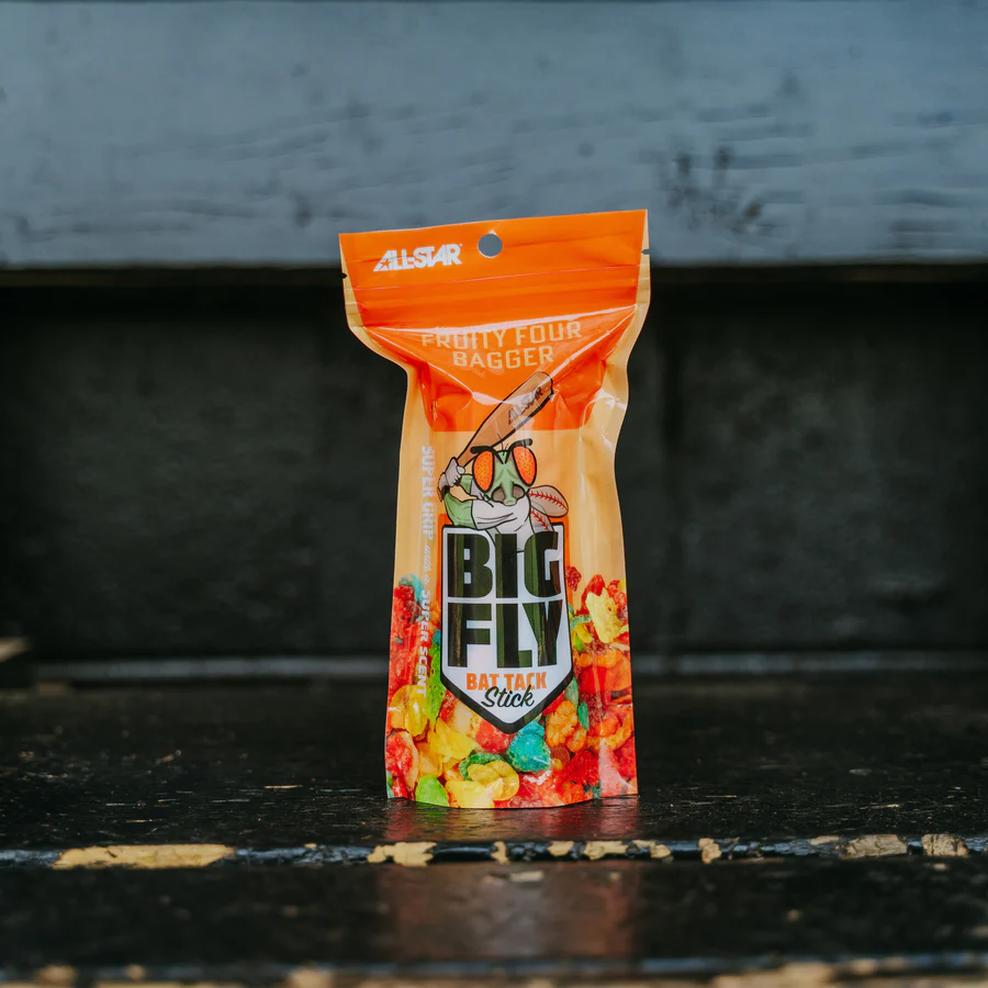 An upright All Star Big Fly Bat Tack Stick (BFST1) in bright, all-star-themed packaging with orange and multicolored cereal-like graphics enhances bat grip, displayed on a weathered wooden surface.