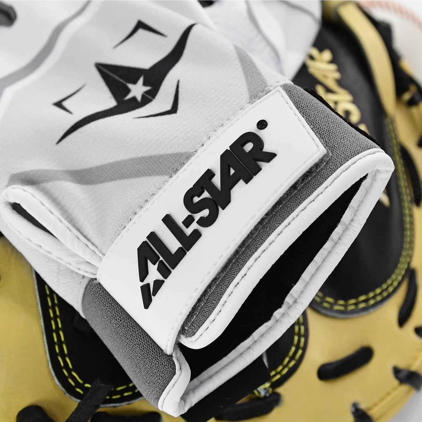 A close-up of the All Star S7 Axis Padded Inner Glove (CG6001) in white, gray, and black, resting on a tan and black leather baseball mitt with yellow stitching.