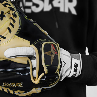 A close-up of a person wearing the All Star S7 Axis Padded Inner Glove (CG6001) and holding a black and tan baseball glove, with part of an All Star logo visible on a black hoodie in the background.