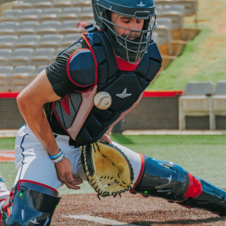 A baseball player, wearing the All Star MVP Pro Catcher's Chest Protector: CPCC-5 that meets NOCSAE standard, catches a ball.
