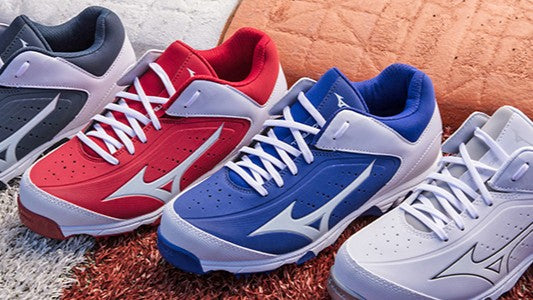 Four pairs of athletic shoes in gray, red, blue, and white are lined up side by side on a textured surface, each featuring a white logo and matching laces.