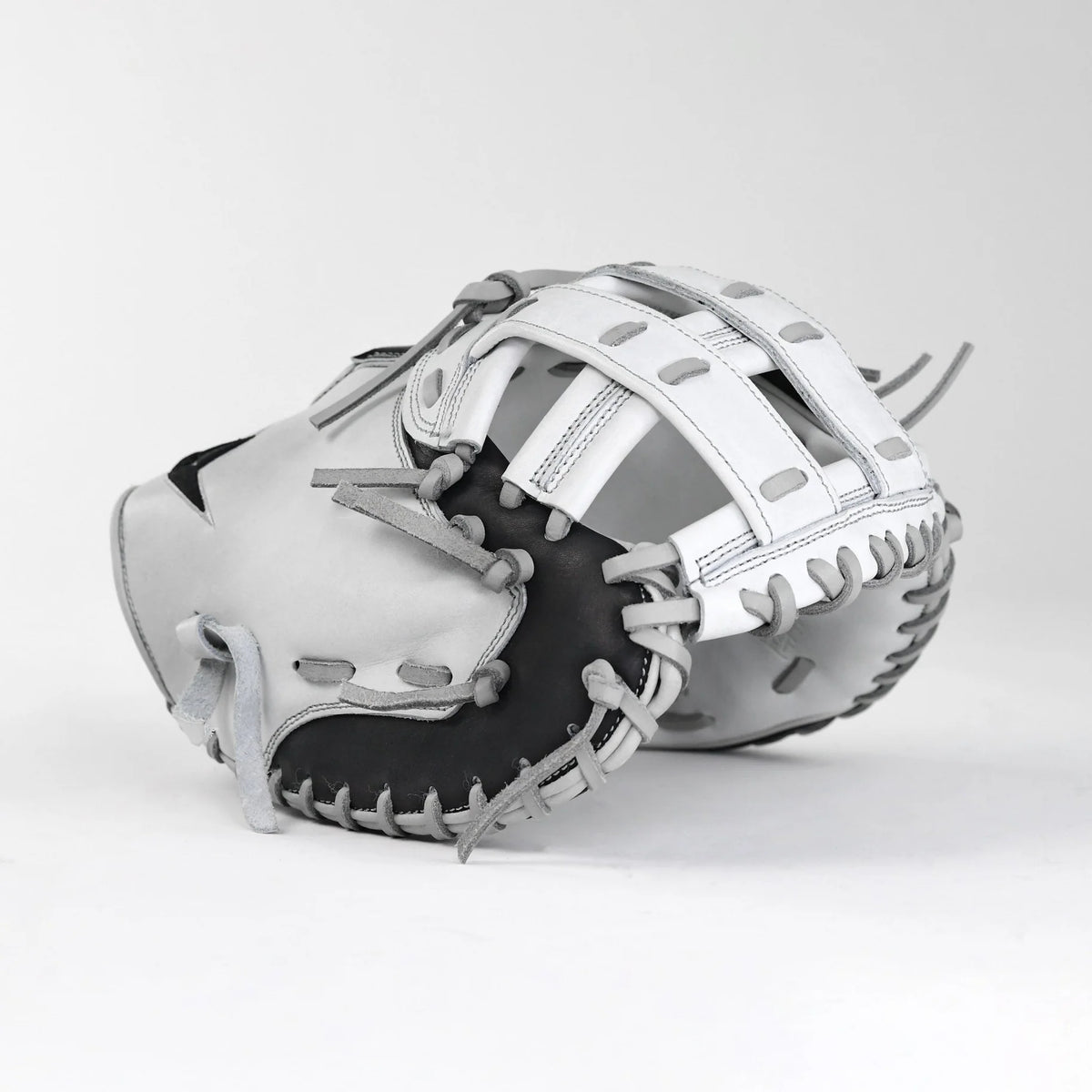 The All Star PHX 33″ Paige Halstead Fastpitch Catcher’s Mitt (CMW-PHX-33) by All Star, featuring a striking white and black design with gray laces, rests on a plain white surface with its pocket and webbing details prominently displayed. Engineered with an adjustable pocket system for an ideal travel ball fit, this mitt seamlessly blends style and performance.