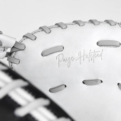 A close-up of the All Star PHX 33″ Paige Halstead Fastpitch Catcher’s Mitt (CMW-PHX-33) showcases its white leather construction with gray laces and “Paige Halstead” embossed on the glove, featuring an adjustable pocket system designed by All Star for a perfect travel ball fit.