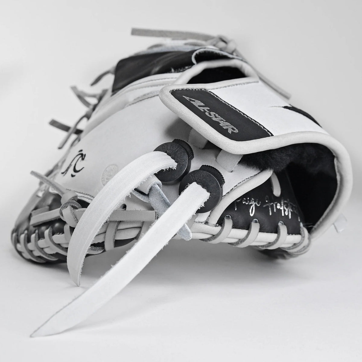 A close-up of the All Star PHX 33″ Paige Halstead Fastpitch Catcher’s Mitt (CMW-PHX-33) in white and black, with visible laces and All Star branding, showcases its adjustable pocket system for a custom travel ball fit against a plain white background.