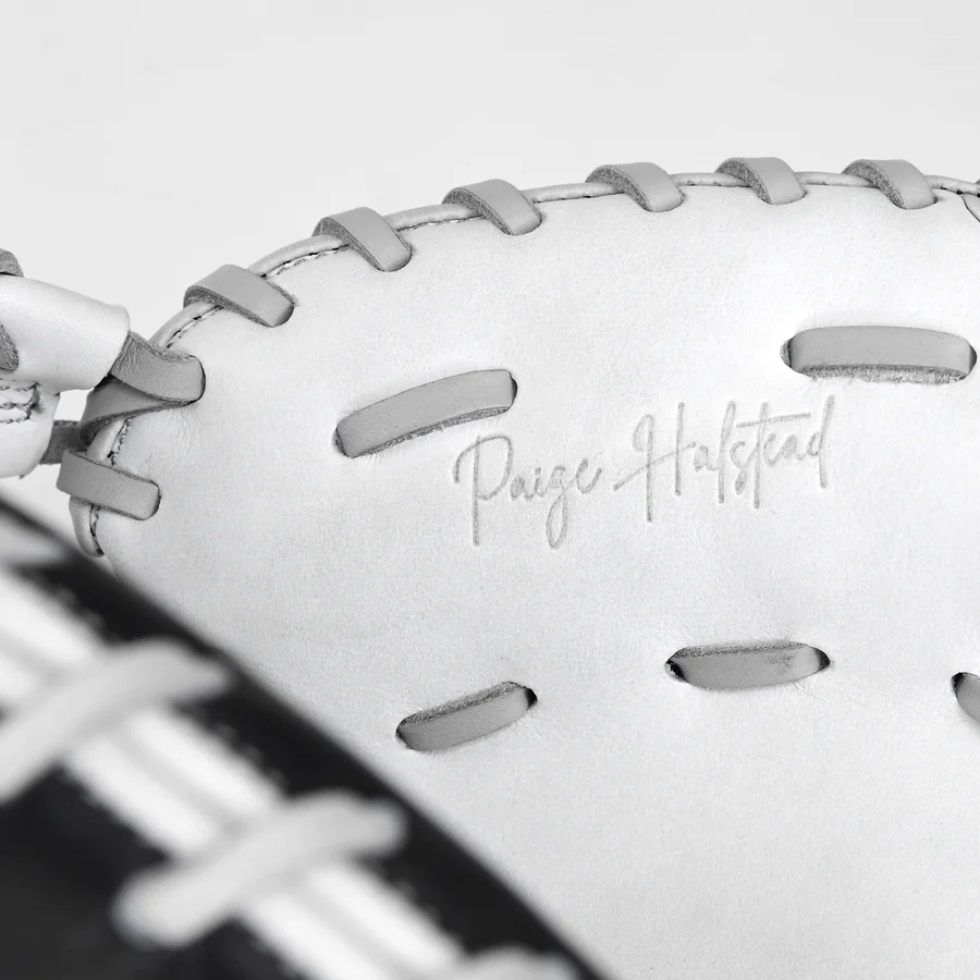 Close-up of the All Star PHX 34" Paige Halstead GM Fastpitch Catcher's Mitt (CMW-PHX-34) with gray laces. "Paige Halstead" is embossed on the premium leather. Part of a black and white striped background appears in the corner.