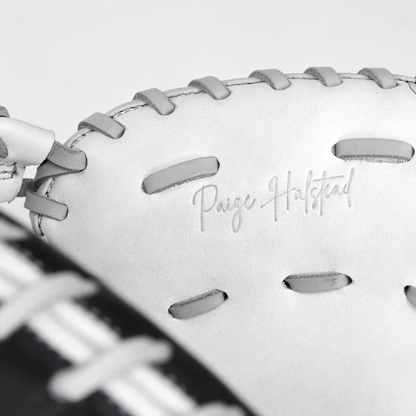 Close-up of the All Star PHX 34" Paige Halstead GM Fastpitch Catcher's Mitt (CMW-PHX-34) with gray laces. "Paige Halstead" is embossed on the premium leather. Part of a black and white striped background appears in the corner.