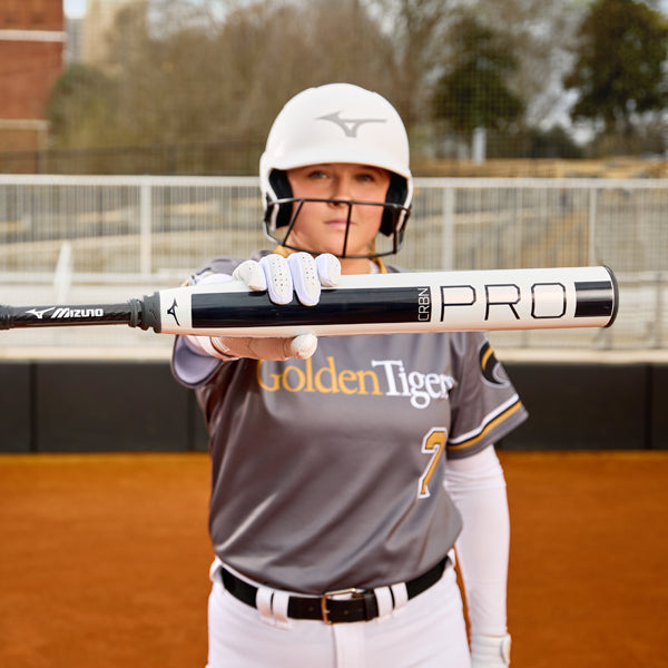 A softball player in a gray Golden Tigers uniform and white helmet holds out a black and white bat labeled PRO toward the camera on an outdoor field.