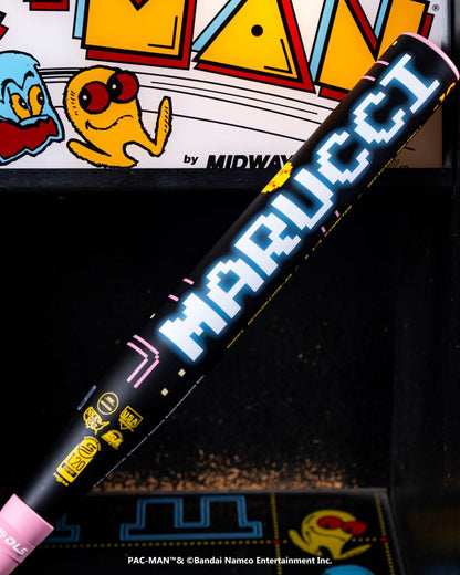 A black 2027 Marucci ASURA Rise PAC-MAN (-10) Fastpitch Softball Bat (MFPASR10PM) lies in front of a PAC-MAN Collection arcade game, with PAC-MAN and ghosts visible on the game's colorful display.