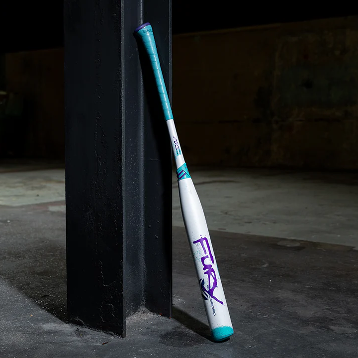 A white and teal baseball bat with Fury written in purple letters leans against a black metal beam in a dimly lit industrial space with a concrete floor.