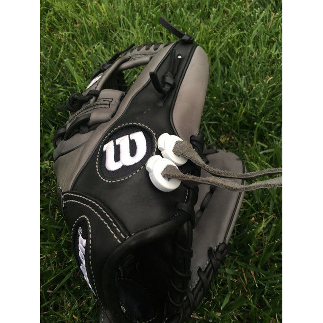 A black and gray Wilson baseball glove with two white All Star GloveLock (4 Pack): GL-4PACK attached by gray strings, resting on green grass to keep the glove secure.